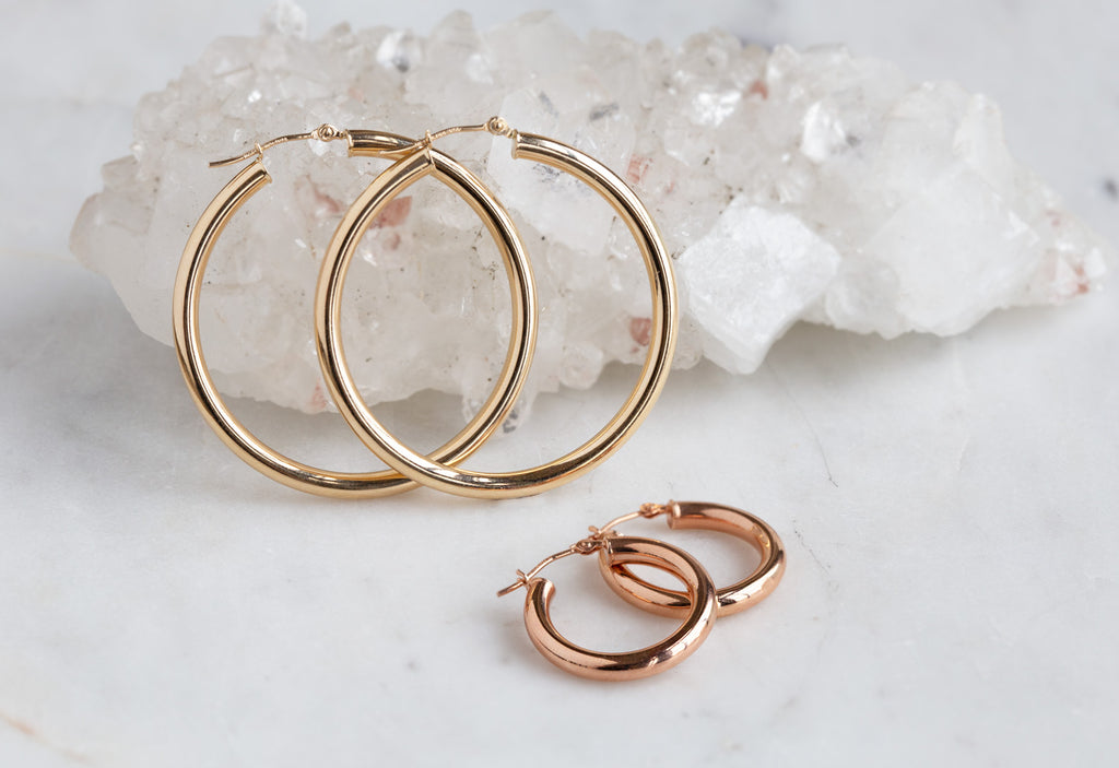 large yellow gold hoops and small rose gold hoops on white marble tile