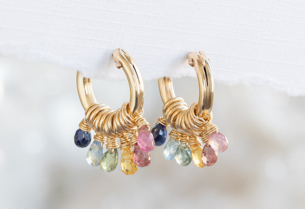 Rainbow Sapphire Hoop Earrings Hanging on Textured White Paper