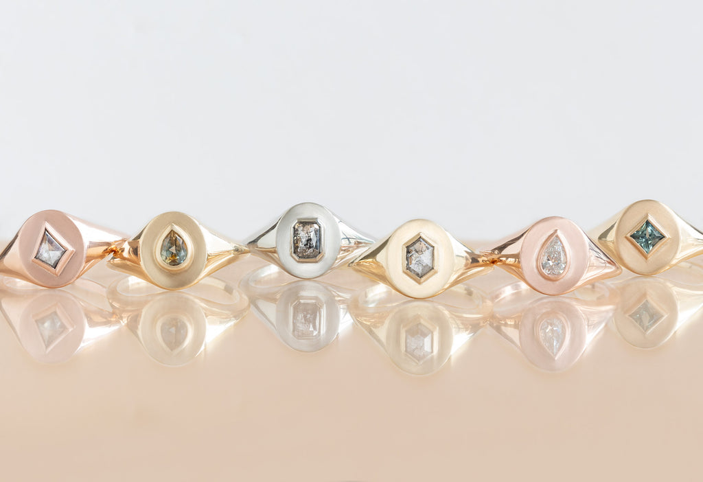  six diamond and gemstone signet rings on peach tile